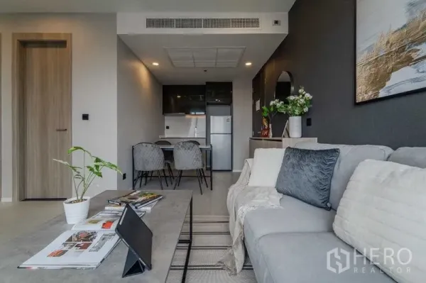 Condominium for rent in Pathum Wan, Bangkok - Sofa seating area looking toward kitchenette and dining set in a neutral gray palette.