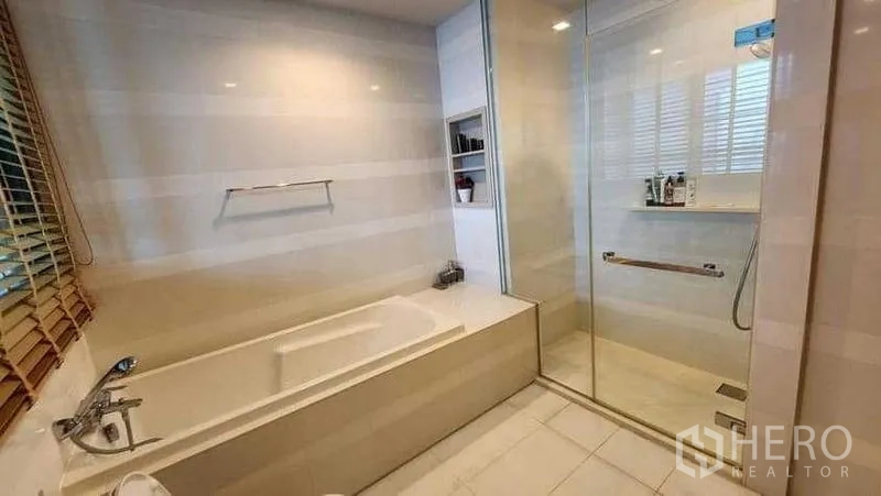 Condominium for rent in Khlong Toei, Bangkok - Bright bathroom with built-in bathtub and glass shower enclosure.