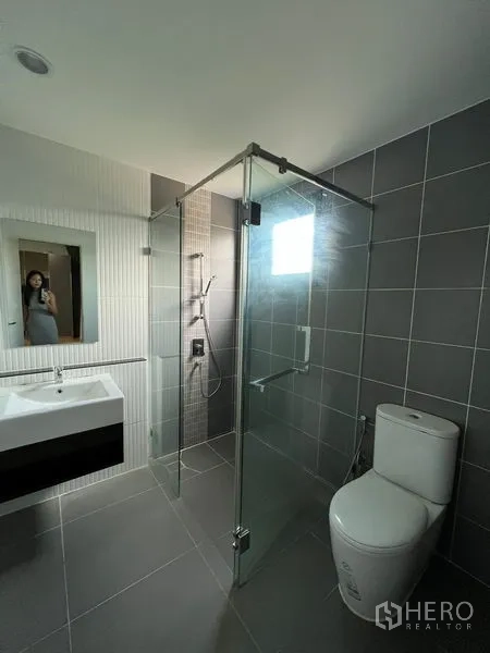 Detached House for rent in Saphan Sung, Bangkok - Modern bathroom with glass-enclosed shower, sink and toilet finished in gray tiles.