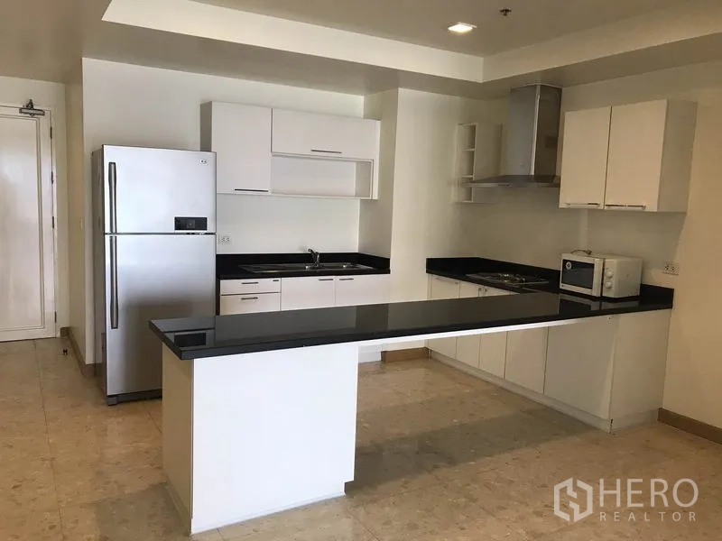 Condominium for rent in Khlong Toei, Bangkok - U-shaped kitchen with white cabinets, stainless refrigerator and extended breakfast island.