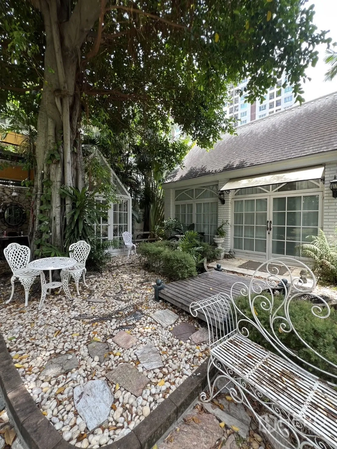 Detached House for rent in Phra Khanong, Bangkok - Shaded courtyard with white wrought-iron table set beside a cottage-style facade.