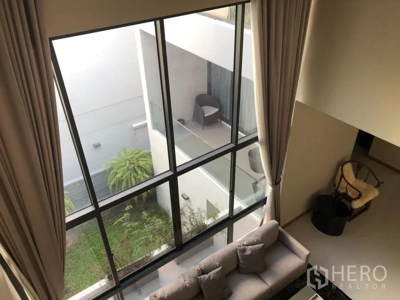 บ้าน ให้เช่าหรือขายในHuai Khwang, Bangkok - โถงรับแขกเพดานสูง ผนังกระจกเต็มบาน มองเห็นลานภายในและระเบียงที่มีต้นไม้
