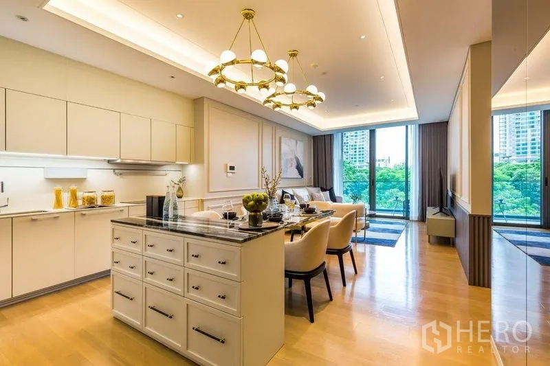 Condominium for rent in Pathum Wan, Bangkok - Open-plan kitchen, dining, and living area with island, chandeliers, and large windows to greenery.