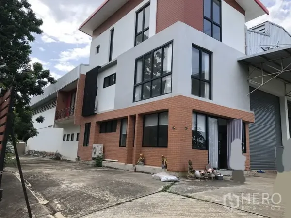 Factory for rent or sale in Lat Lum Kaeo, Pathum Thani - Side view of the factory building showing large windows, brick facade and adjacent roller shutter.