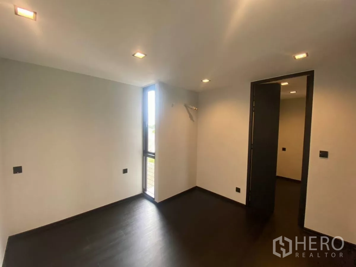 Townhouse for rent in Huai Khwang, Bangkok - Compact bedroom with recessed lights, dark floor and a slim corner window.