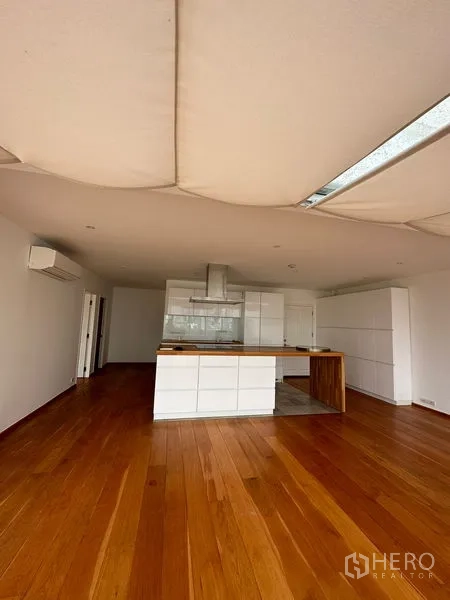Condominium for rent in Khlong Toei, Bangkok - Open-plan area with white kitchen, island cooktop and warm wood flooring.