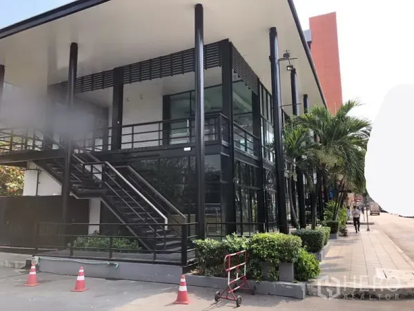 Retail Space for rent in Khlong Toei, Bangkok - Side view of retail unit with black steel frame, external staircase, large windows and sidewalk greenery.