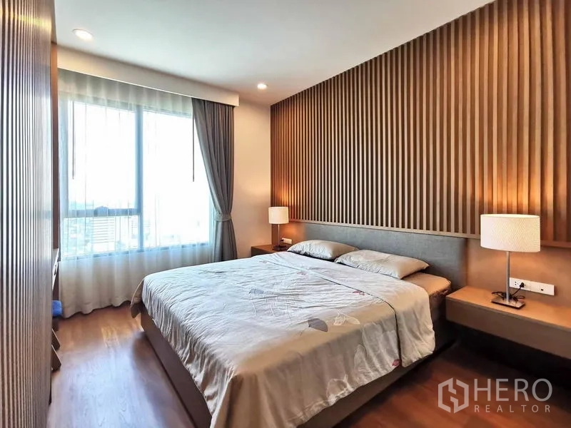 Condominium for rent in Sathon, Bangkok - Bedroom with wooden slat accent wall, bedside lamps and a wide window.