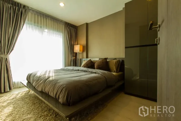 Condominium for rent or sale in Sathon, Bangkok - Warm bedroom with large bed, floor-to-ceiling curtains, soft lighting and a built-in wardrobe.