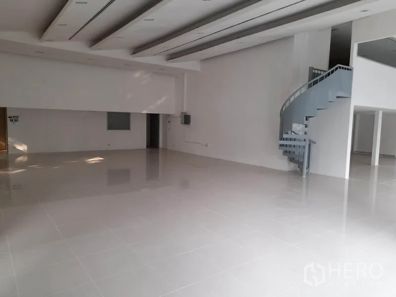 零售空间 出租在Ratchathewi, Bangkok - 挑高展厅，设弧形楼梯通往夹层，整体白色精装。