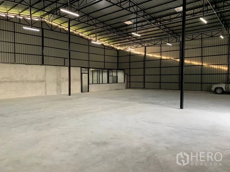 Warehouse for rent in Khan Na Yao, Bangkok - Open-plan warehouse space with office windows, steel truss roof, and polished concrete floor.
