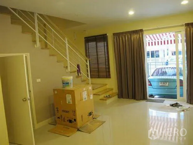 联排别墅 出租或出售在Wang Thonglang, Bangkok - 一层起居区带楼梯，推拉玻璃门通向车棚，深色窗帘。