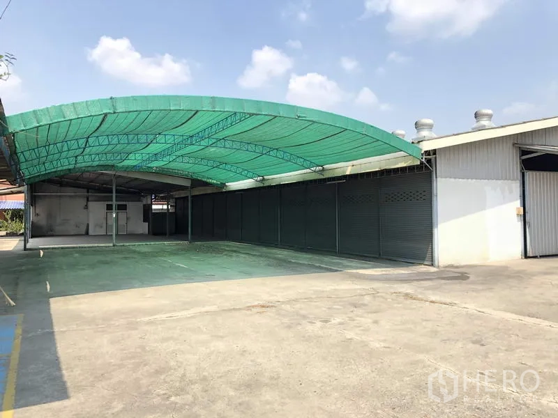 货栈 出租在Khlong Luang, Pathum Thani - 带绿色遮棚的装卸区，旁侧设多组卷帘门。