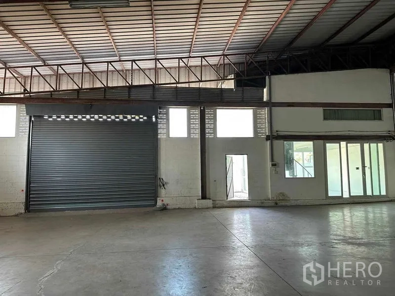 Warehouse for rent in Nakhon Pathom - Spacious warehouse interior with high steel-truss roof, polished concrete floor and a large roller shutter door.