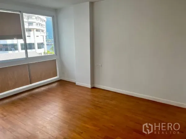 Condominium for rent in Bang Kho Laem, Bangkok - Spacious bedroom with large window, natural light, and wood floors overlooking nearby buildings.