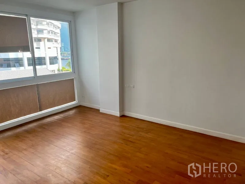 Condominium for rent in Bang Kho Laem, Bangkok - Spacious bedroom with large window, natural light, and wood floors overlooking nearby buildings.