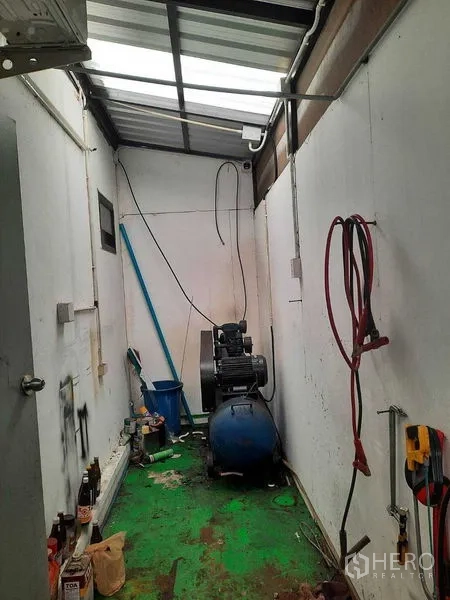 Warehouse for sale in Samut Prakan - Narrow utility room with an air compressor under a translucent roof panel.