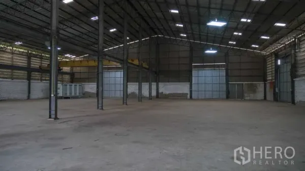 Factory for rent in Bang Phli, Samut Prakan - Spacious warehouse interior with high steel truss roof, concrete floor and large roller doors.
