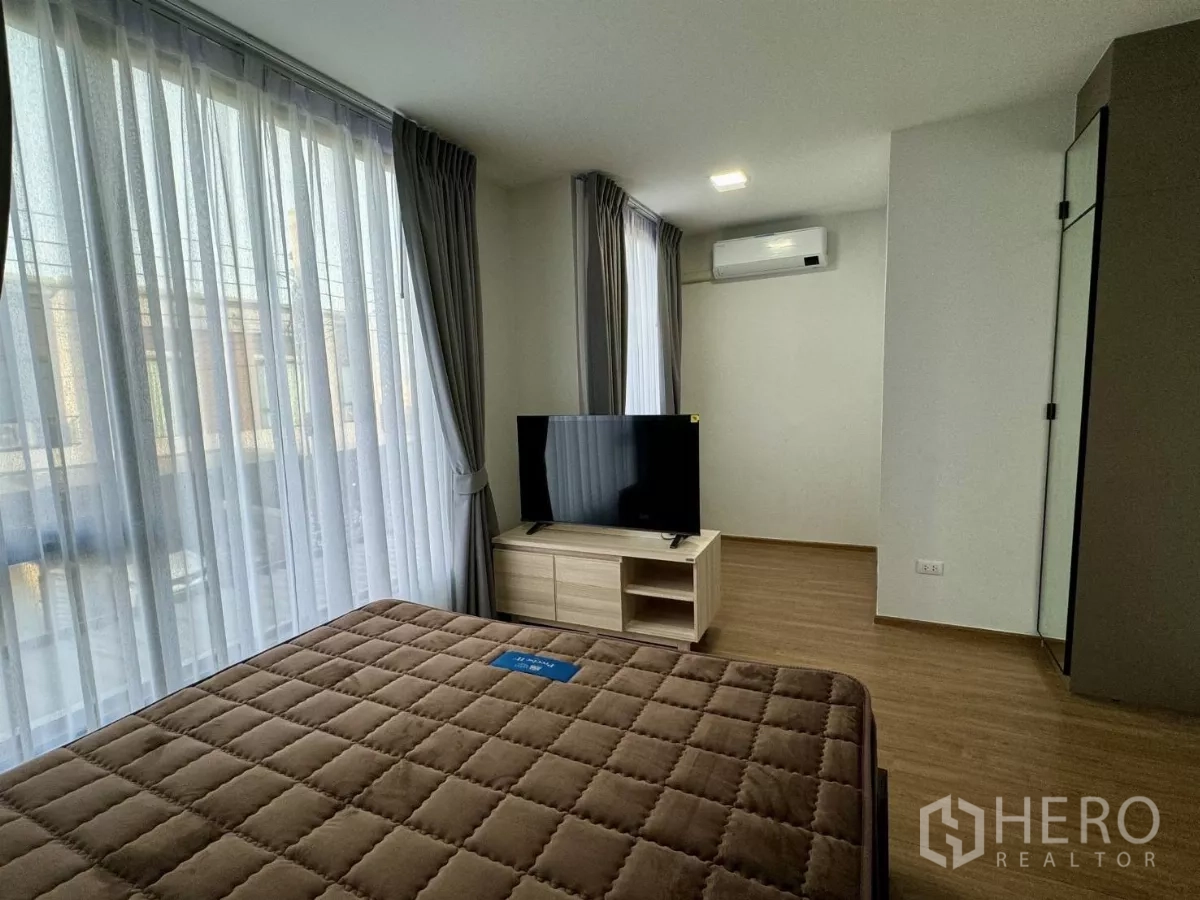 Townhouse for rent in Bang Phli, Samut Prakan - Spacious bedroom with brown quilted mattress, corner windows and TV stand