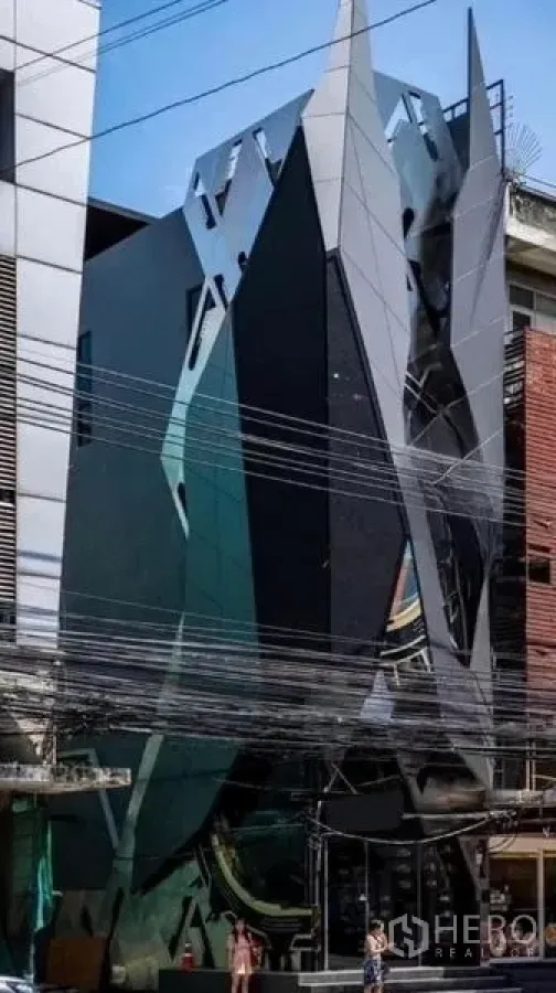 Shophouse for rent in Khlong Toei, Bangkok - Street view of multi-storey shophouse with shard-like facade and glass panels.