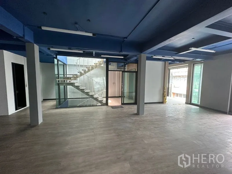 办公空间 出租在Watthana, Bangkok - 开放式写字楼，蓝色天花与木纹地板，中央为玻璃楼梯井。