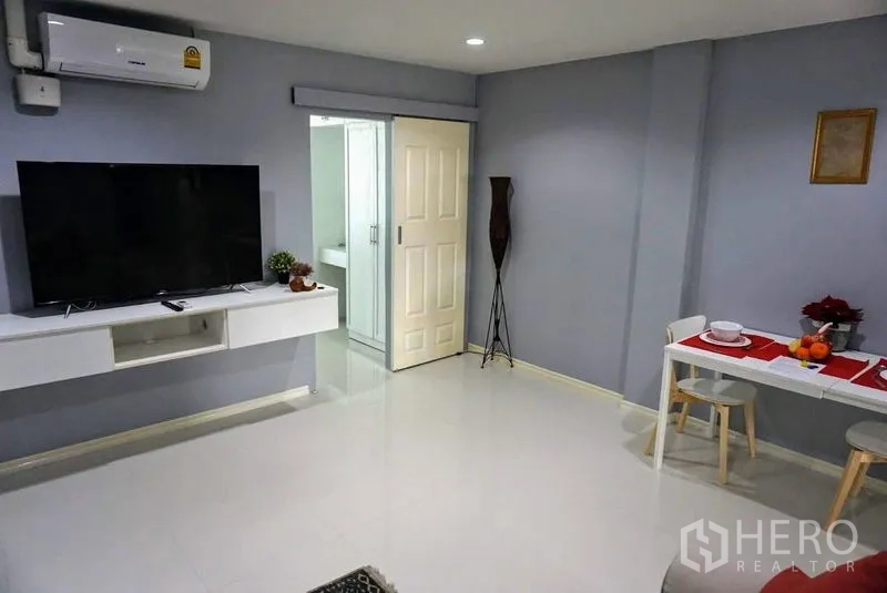 Shophouse for sale in Phra Khanong, Bangkok - Open-plan living area with wall-mounted TV, compact dining nook and a doorway to the bathroom.