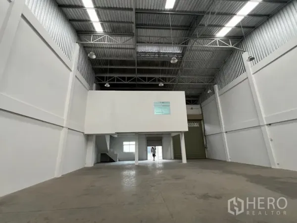 Warehouse for rent in Phra Samut Chedi, Samut Prakan - Wide storage bay under the mezzanine with metal roof and bright industrial lighting.