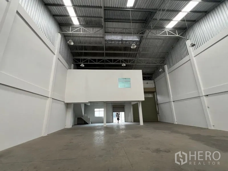 Warehouse for rent in Phra Samut Chedi, Samut Prakan - Wide storage bay under the mezzanine with metal roof and bright industrial lighting.