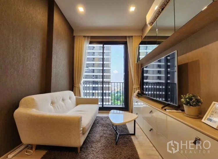 คอนโด ให้เช่าในWatthana, Bangkok - มุมห้องนั่งเล่นหันสู่ระเบียง โซฟาสีครีมและชั้นวางทีวีบิวท์อิน