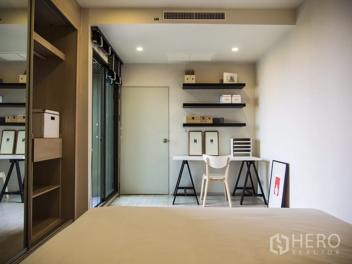 Condominium for rent in Watthana, Bangkok - Bedroom with study nook, sliding glass doors and wall-mounted shelves.