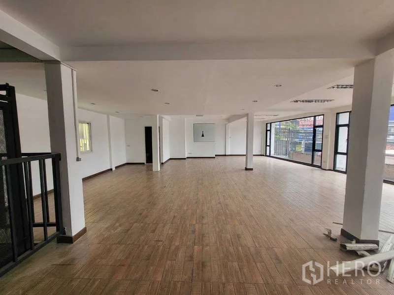 Shophouse for rent in Khlong Toei, Bangkok - Bright open-plan upper level with floor-to-ceiling glass, multiple columns, and wood-look floors.