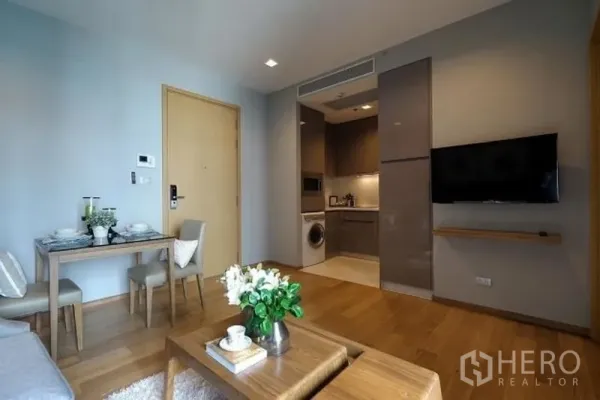 公寓 出租在Watthana, Bangkok - 开放式客厅，正对配备洗衣机的厨房，墙挂电视与紧凑餐桌。