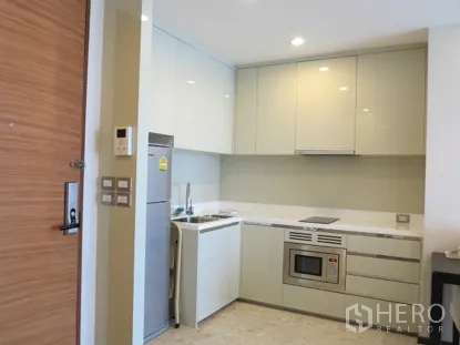 Condominium for rent in Khlong Toei, Bangkok - Compact modern kitchen with glossy cabinets, built-in oven, electric cooktop, sink, and refrigerator.