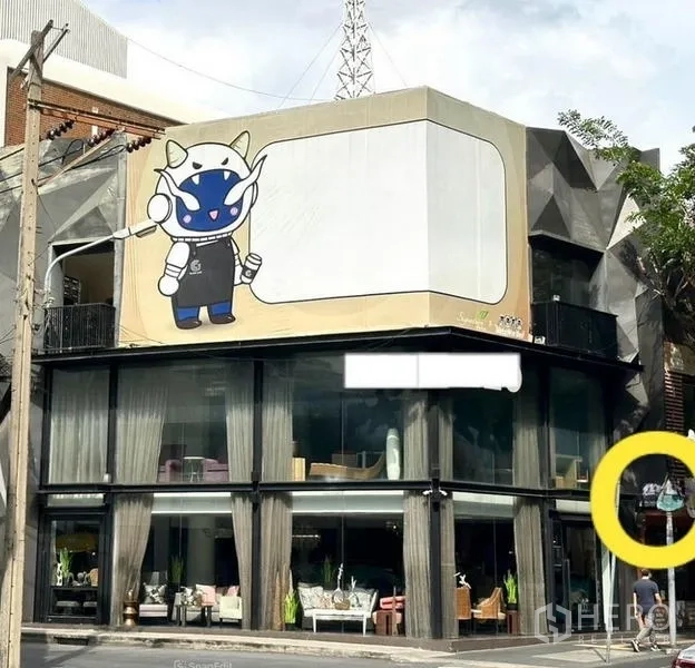 Shophouse for rent in Watthana, Bangkok - Street view of a modern shophouse showroom with floor-to-ceiling windows and a large signage panel near BTS Phrom Phong.