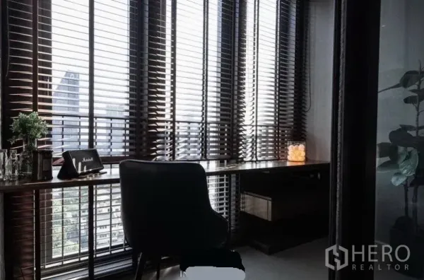 Condominium for rent in Khlong Toei, Bangkok - Corner study with long built-in desk by floor-to-ceiling windows and skyline views through venetian blinds.
