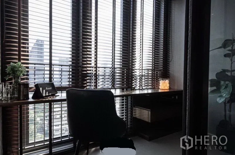 Condominium for rent in Khlong Toei, Bangkok - Corner study with long built-in desk by floor-to-ceiling windows and skyline views through venetian blinds.