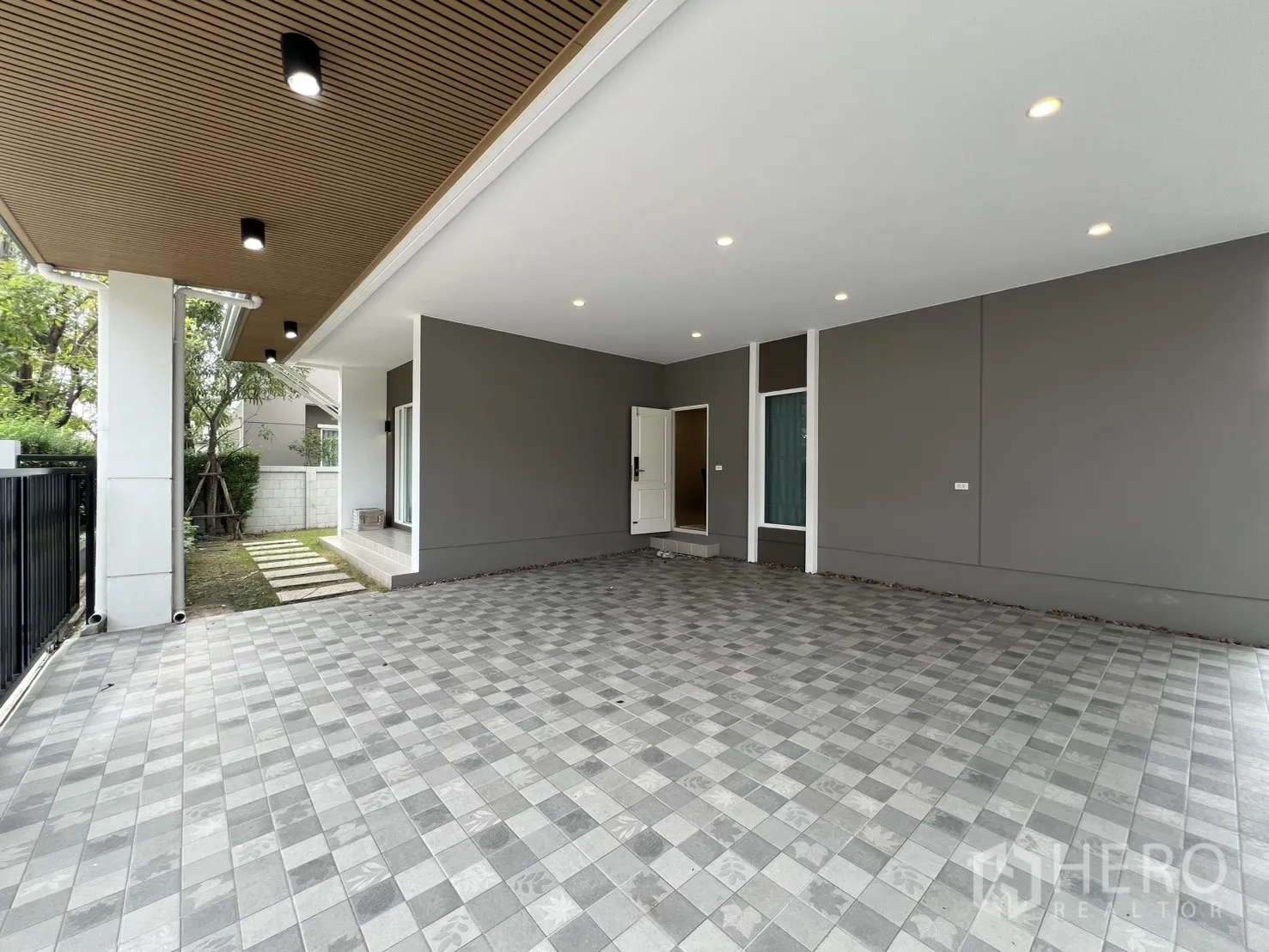独栋房屋 for rent in Lat Krabang, Bangkok - 有顶车位铺灰色地砖，木格栅天花与筒灯，旁侧小草坪与入户台阶。