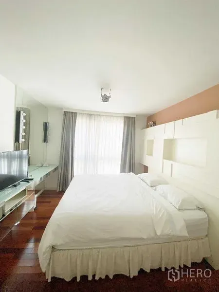 Condominium for rent in Watthana, Bangkok - Light-filled bedroom with large bed, built-in shelving, TV console, and sheer floor-to-ceiling curtains.