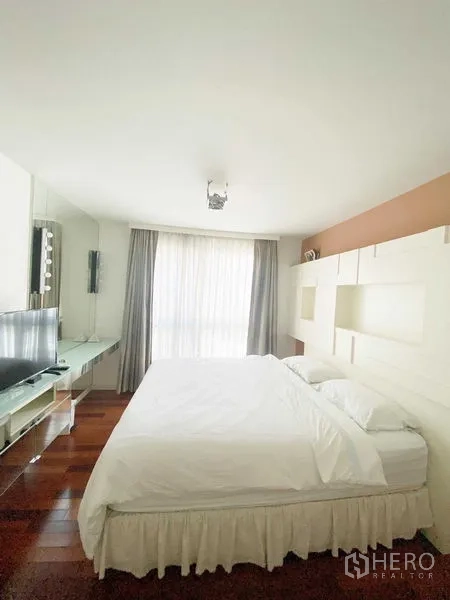 Condominium for rent in Watthana, Bangkok - Light-filled bedroom with large bed, built-in shelving, TV console, and sheer floor-to-ceiling curtains.