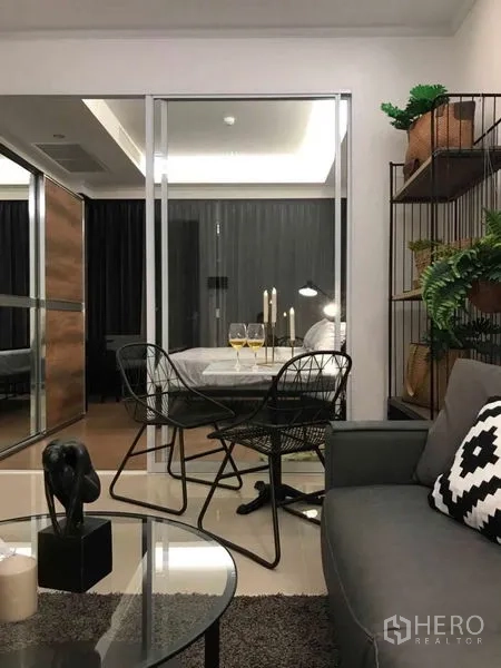 公寓 出租或出售在Ratchathewi, Bangkok - 客厅与餐区一体，玻璃隔断通向卧室，铁艺椅与灰色沙发。