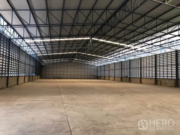 Warehouse for rent in Khlong Sam Wa, Bangkok - Spacious warehouse interior with high steel-truss roof, louvered ventilation walls, and smooth concrete floor lit by translucent roof panels.