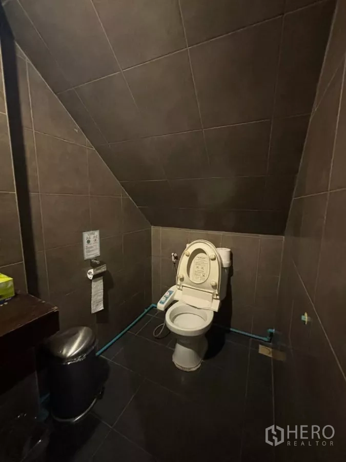 店屋 出租在Watthana, Bangkok - 楼梯下深色瓷砖卫生间，马桶与垃圾桶。