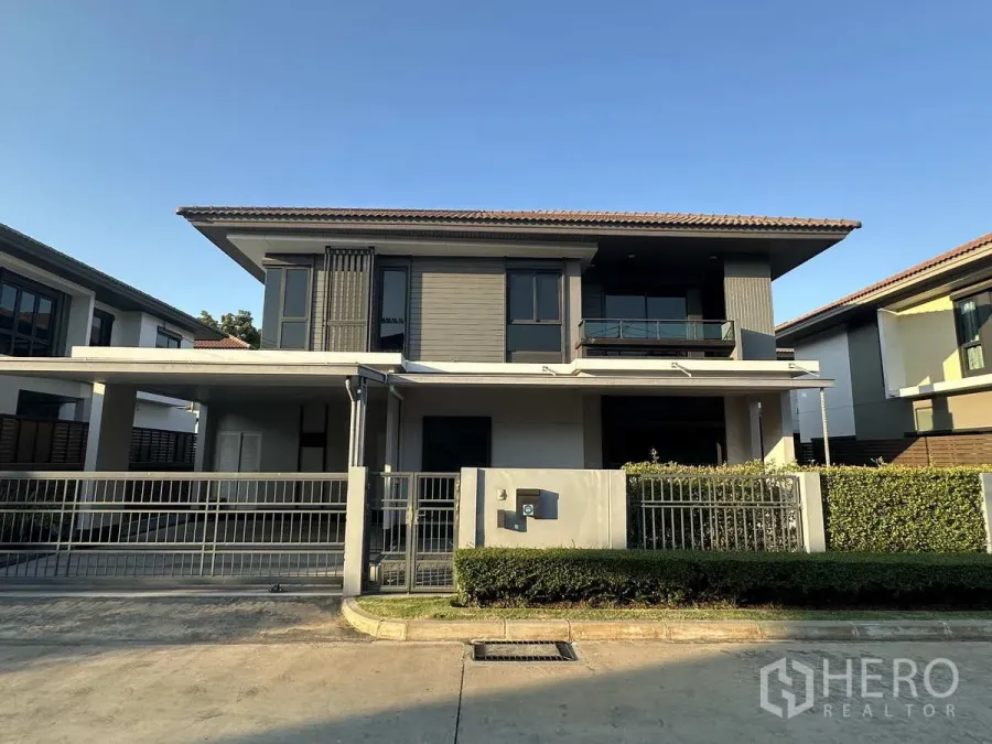Detached House for rent or sale in Lam Luk Ka, Pathum Thani - Modern two‑storey detached house with gated driveway, balcony and landscaped hedge.