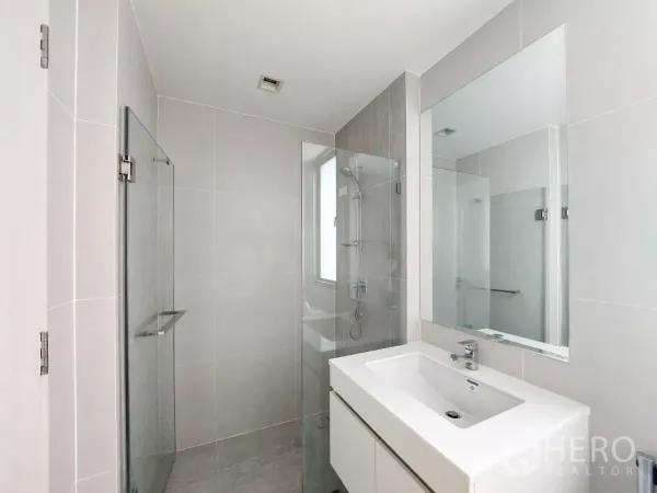 Townhouse for rent in Lat Phrao, Bangkok - Contemporary bathroom featuring a glass-enclosed shower, large mirror and sleek white vanity.
