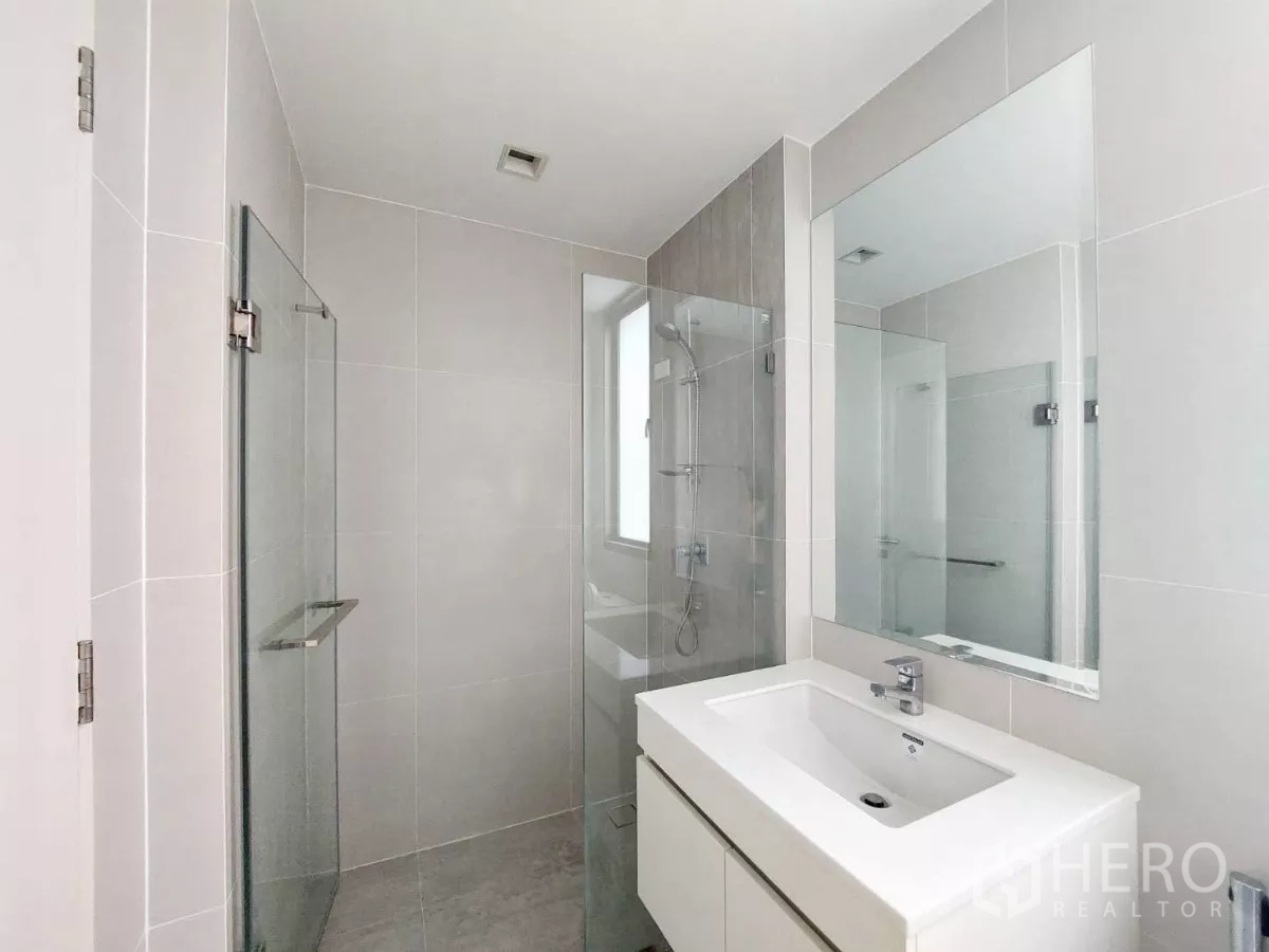 Townhouse for rent in Lat Phrao, Bangkok - Contemporary bathroom featuring a glass-enclosed shower, large mirror and sleek white vanity.