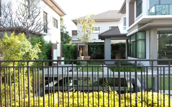 Detached House for rent or sale in Prawet, Bangkok - Landscaped garden with pond and bridge behind a black fence, flanked by neighboring houses.