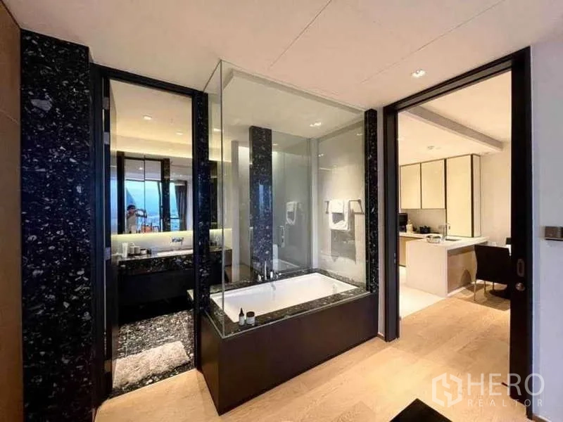 Condominium for rent or sale in Khlong Toei, Bangkok - Luxurious bathroom with glass-enclosed soaking tub and black marble accents.
