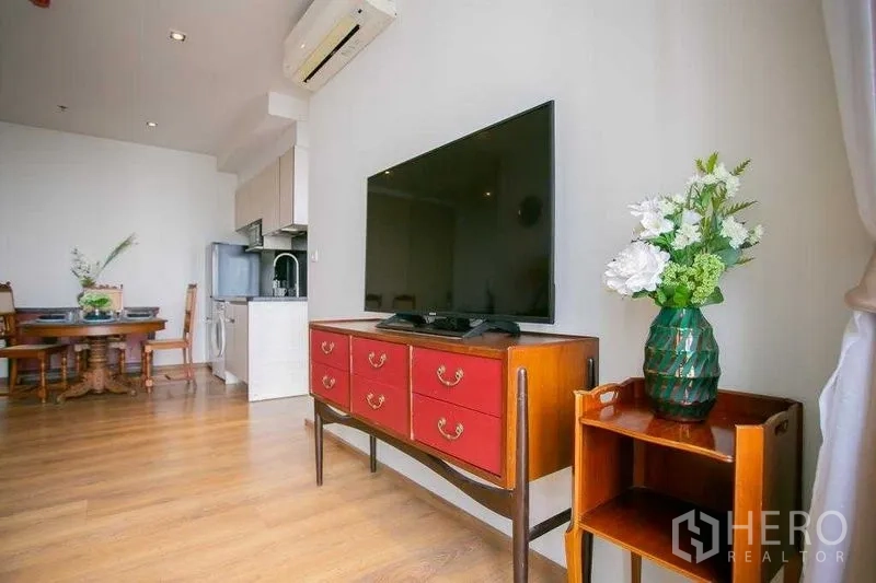 Condominium for sale in Khlong Toei, Bangkok - TV on a vintage red console beside a small side table and vase in the living room.