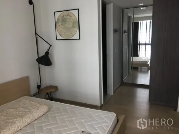 Condominium for rent in Watthana, Bangkok - Bedroom view showing mirrored wardrobe, bedside lamp and door to bathroom.