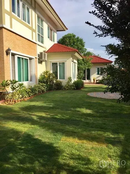 独立式住宅 出售在Pak Kret, Nonthaburi - 房屋侧面，红色瓦顶与宽阔的景观草坪。
